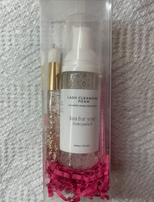 Lash cleansing foam in a clear packaging with pink tissue paper on a textured gray background